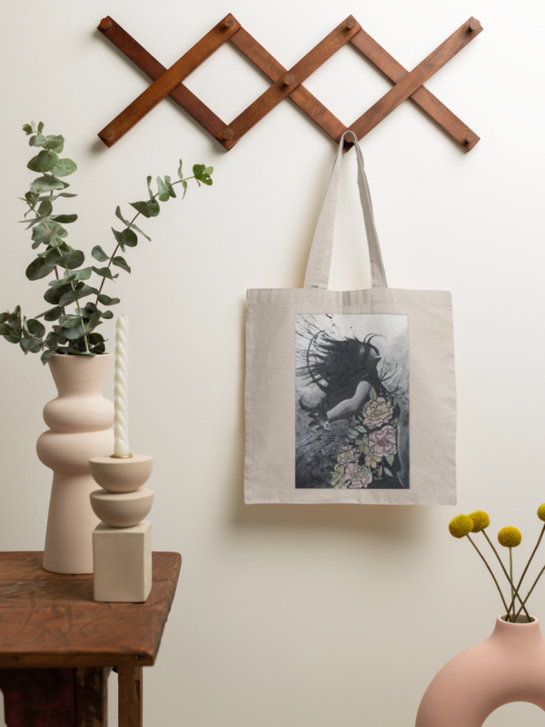 Neutral-colored canvas tote bag with fantasy-style artwork, hanging as home decor.