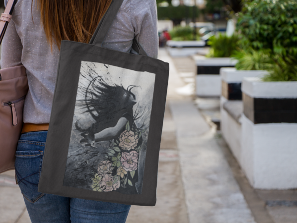 Woman carrying a black canvas tote bag with fantasy-inspired artwork while walking in the city.